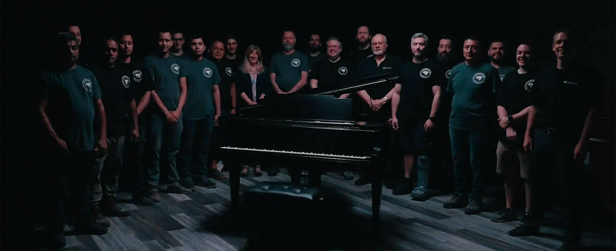 Lindeblad Piano's team, with 25 craftsmen and 10 admin, together smiling around a piano, ready to serve families around the country