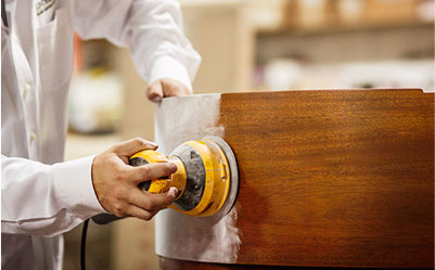 Technician using a sander on a piano case.
