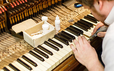 Technician performing detailed work on a partly disassembled piano keyboard.