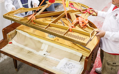 Several technicians hoisting the cast iron harp out of a piano.